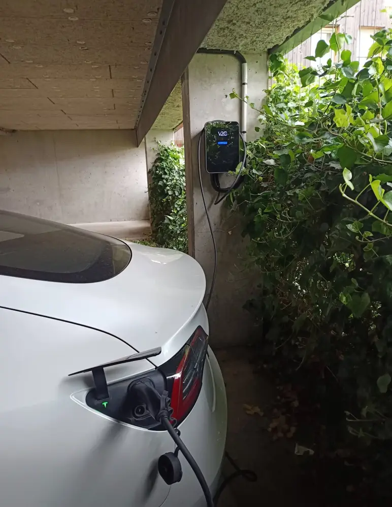 Tesla blanche en charge sur borne V2C dans un carport