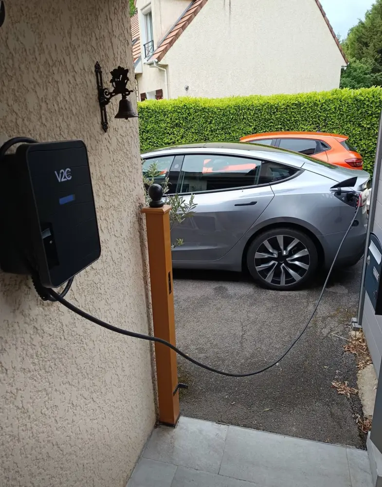 Borne V2C en façade de maison avec Tesla grise en charge