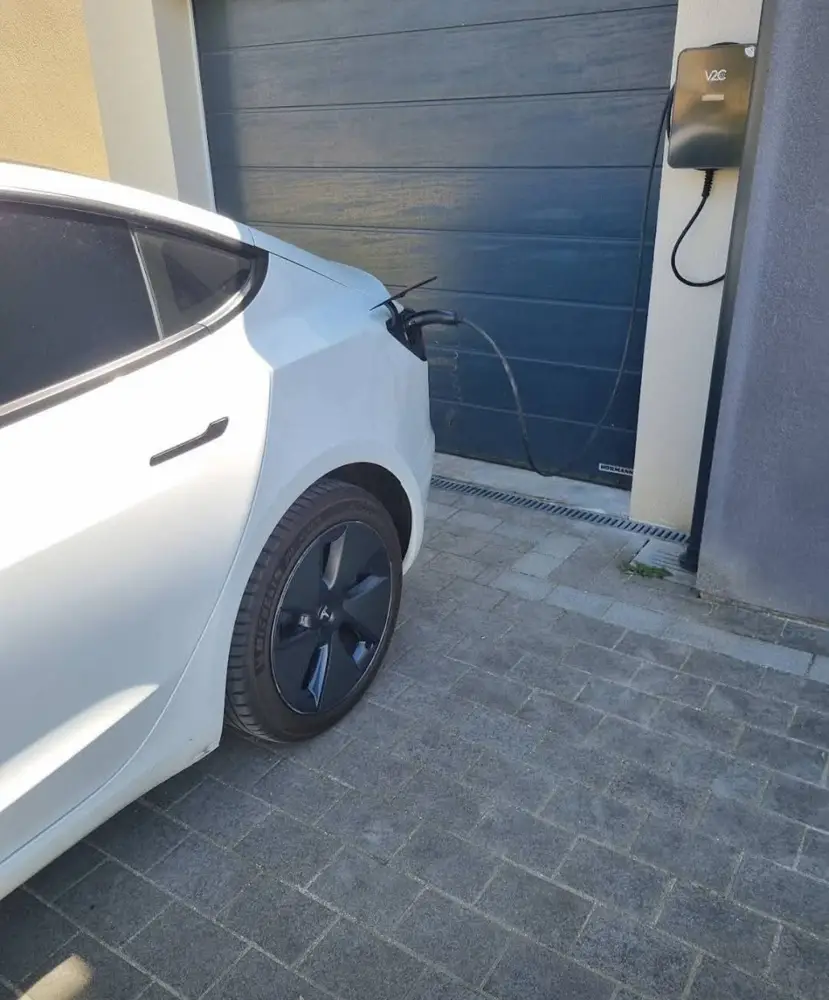 Tesla Model 3 en charge sur une borne V2C posée contre un mur de garage