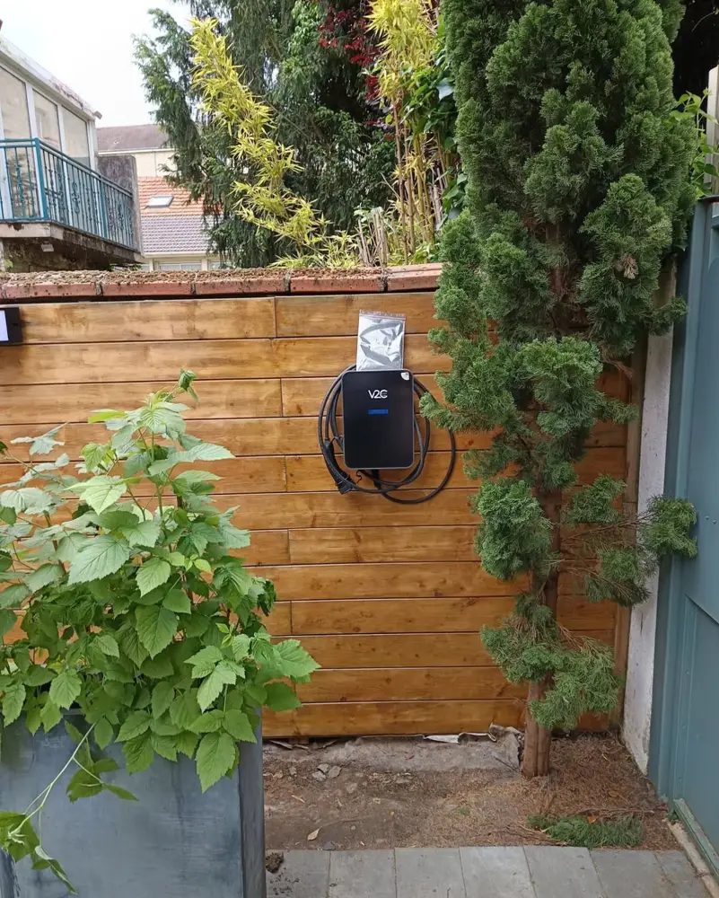 Borne V2C Trydan fixée sur un bardage bois dans un jardin